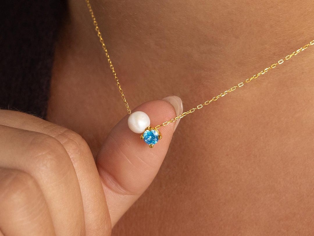 CaitlynMinimalist freshwater pearl beside a blue birthstone on a fine gold chain