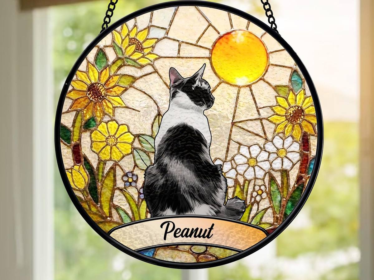 Round printed suncatcher of a black-and-white cat among sunflowers with the cat's name, hanging in a window