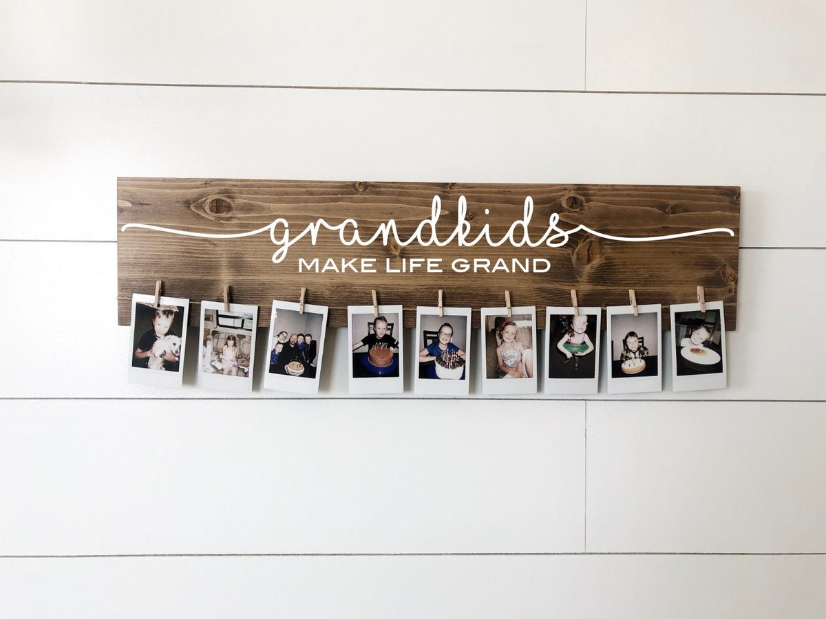 Dark-stained wooden grandkids sign holding nine photographs on mini wooden clothespins, a Christmas gift for grandma