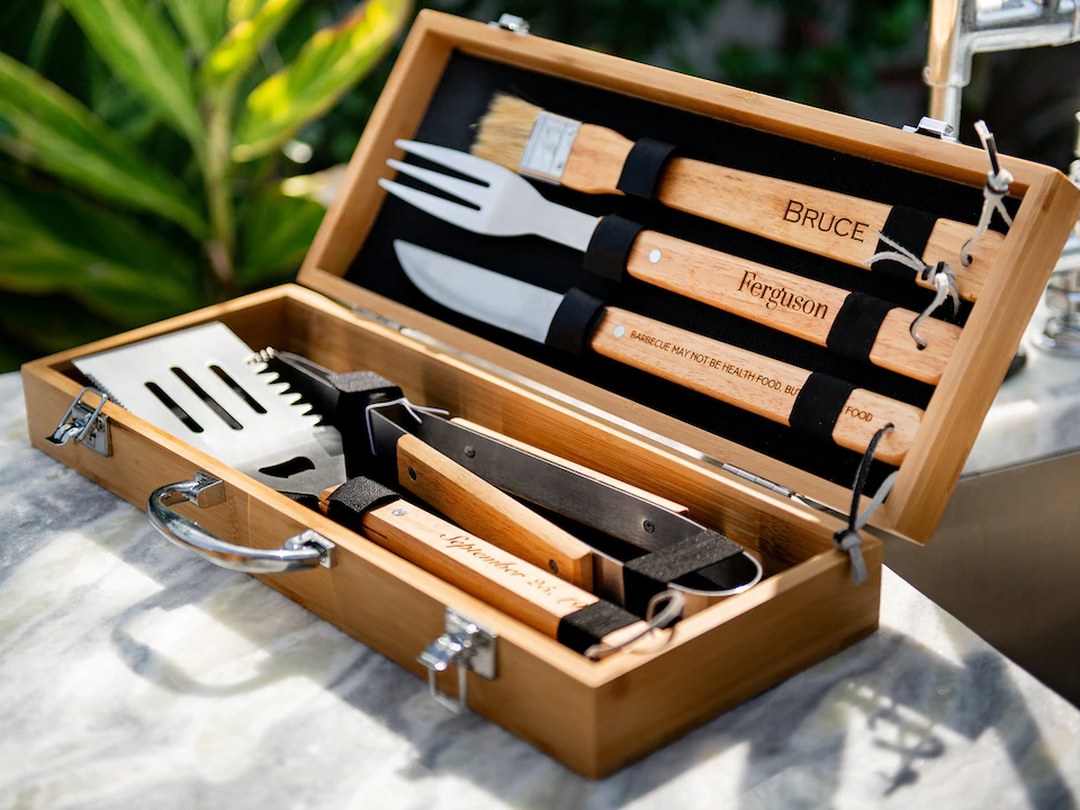 Barbecue tool set with engraved handles in an open wooden storage case