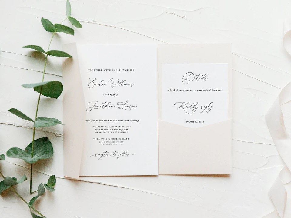 Blush pocket-fold wedding invitation with script lettering beside eucalyptus leaves on white plaster