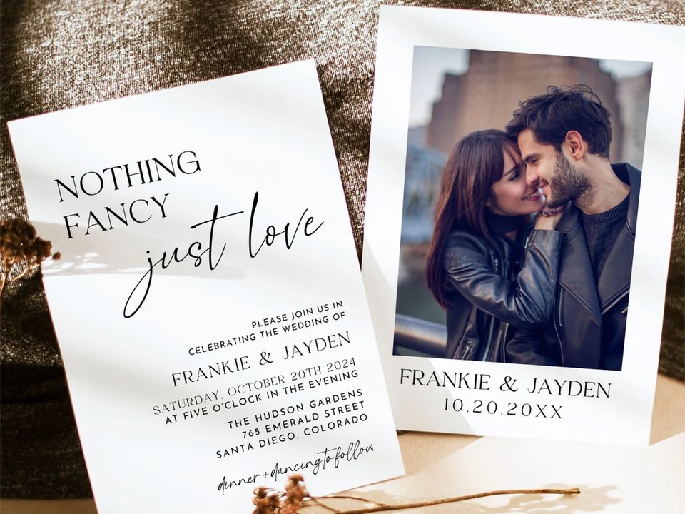 Black script wedding invitation card beside a photo card with a couple's portrait on dark fabric
