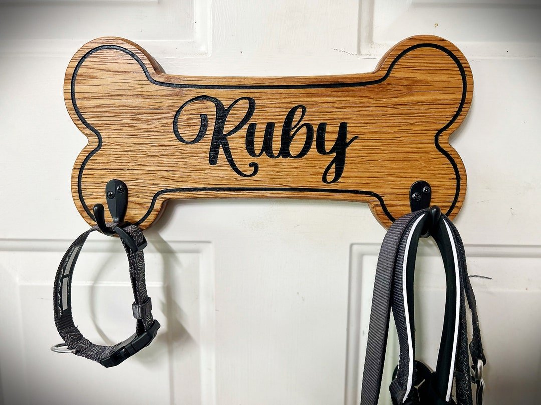 Carved solid oak leash holder shaped like a dog bone, mounted on a wall with leashes hanging