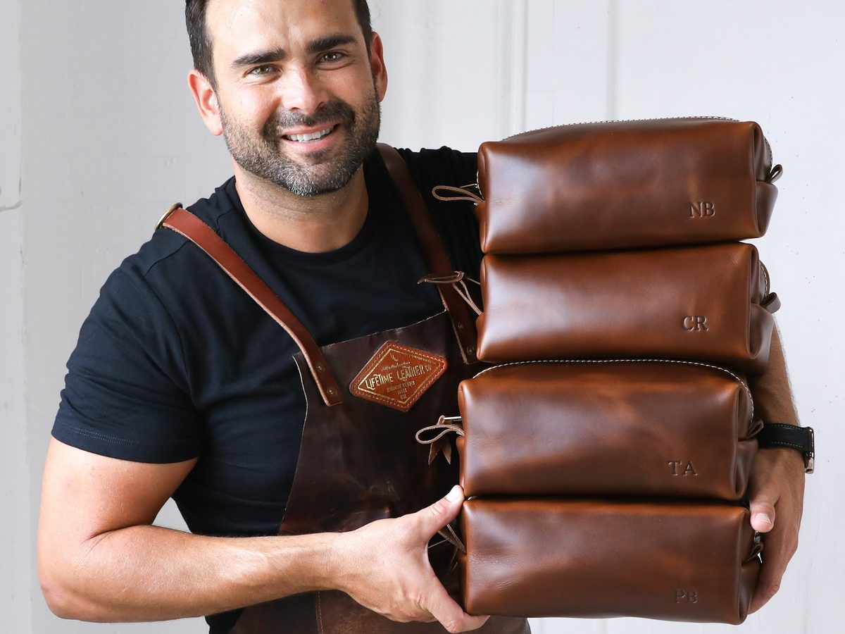 LifetimeLeatherCo brown leather dopp kits with initials, stacked in a leather worker's arms, on Etsy