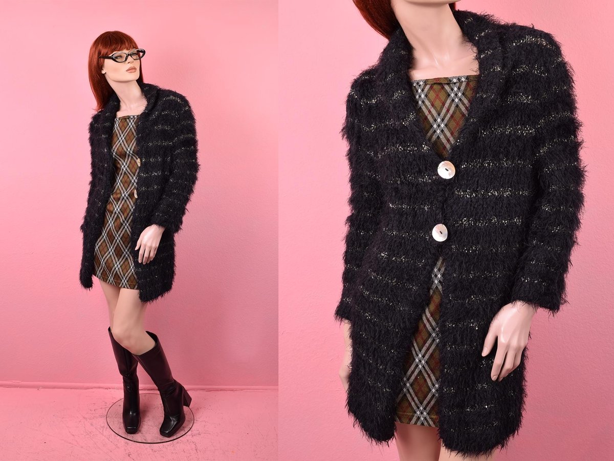 Fuzzy black cardigan with metallic gold stripes over a plaid mini dress on a mannequin, pink backdrop