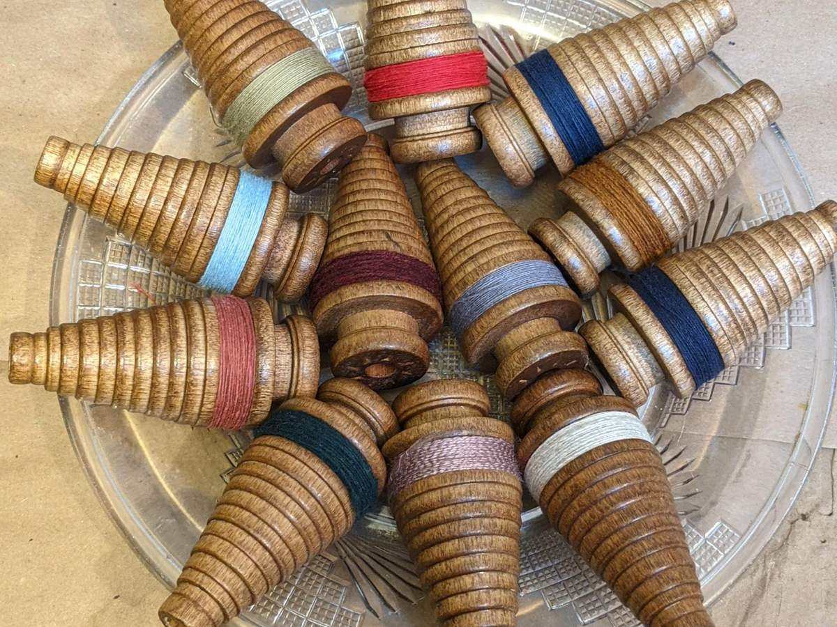 Twelve wooden textile bobbins wound with red, blue and teal thread in a pressed glass dish