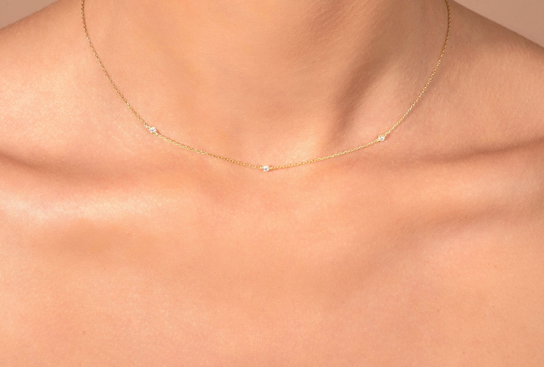 Fine gold chain necklace with three small diamonds set along it, worn at the collarbone