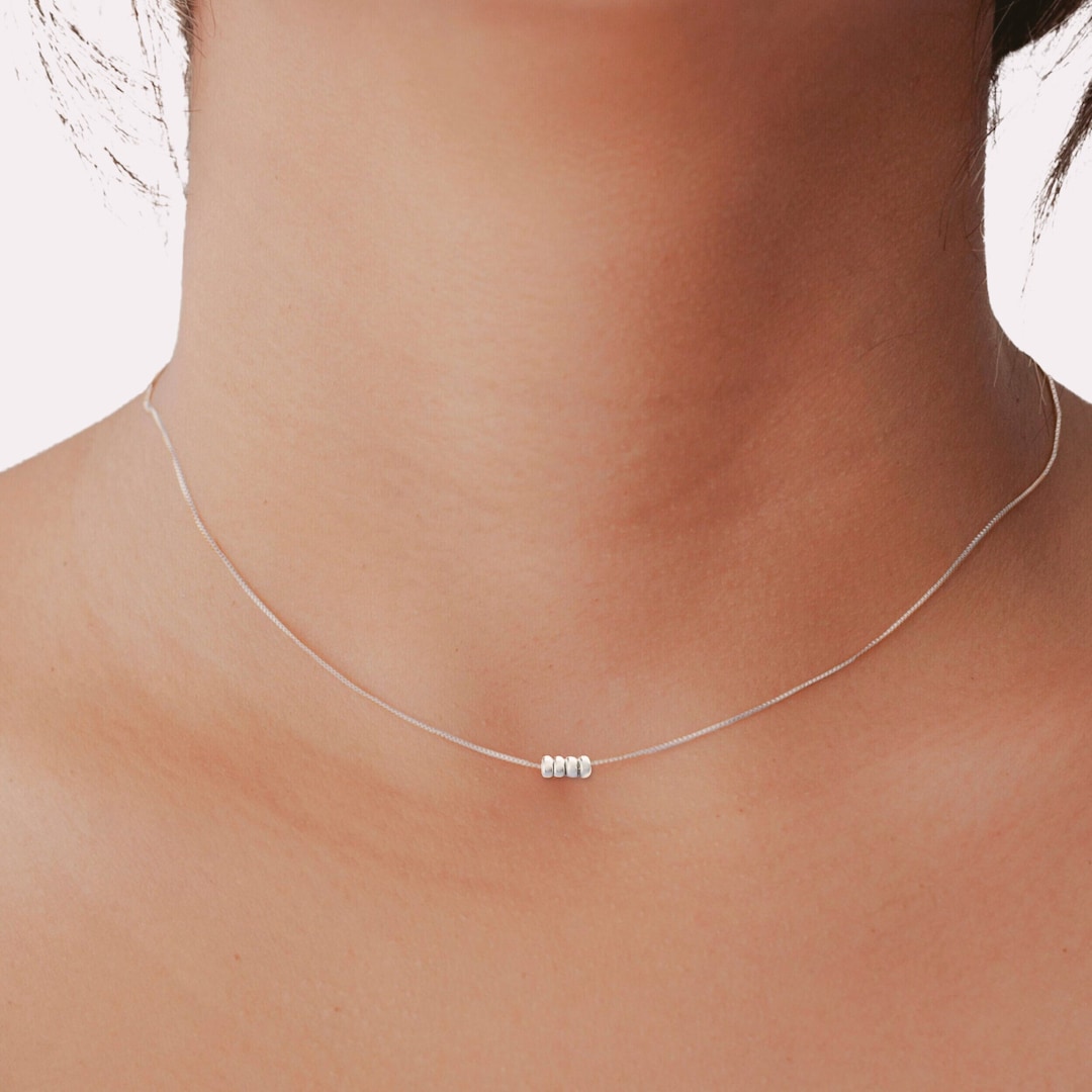Minimalist sterling silver necklace with four small beads on a fine chain